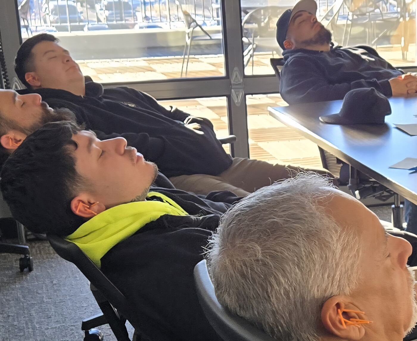 Employees seated fully clothed in a conference room during a group ear acupuncture session